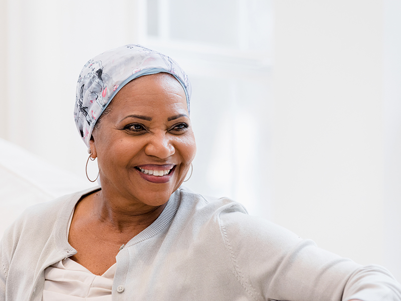 A woman in a head wrap smiles while sitting on a couch