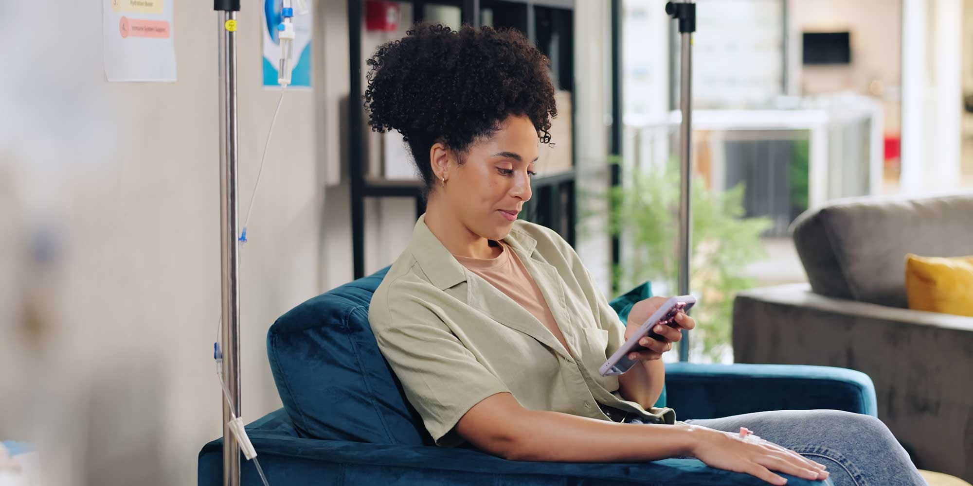 A woman recieves infusion therapy in an office. She's browsing on her phone.
